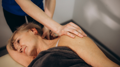 A therapist giving a shoulder massage to an older woman lying on a treatment table, promoting relaxation and wellness.