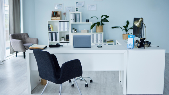 A modern office space featuring a white desk with a laptop, a black ergonomic chair, and a cozy armchair in the corner, surrounded by potted plants and organized shelves, ideal for productivity.