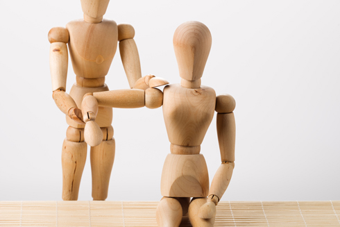 Two wooden mannequin figures, one standing and assisting the other who is seated, showcasing a moment of support or guidance. Ideal for expressive wooden art or figures.