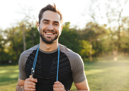 smiling man in athletic wear holding a fitness rope in a park, enjoying a workout session