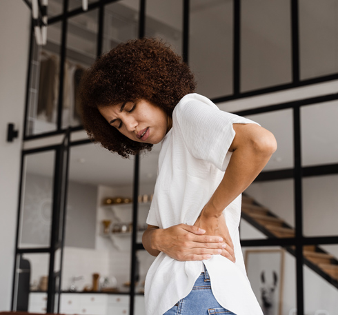 Woman experiencing back pain while standing in a modern home interior.