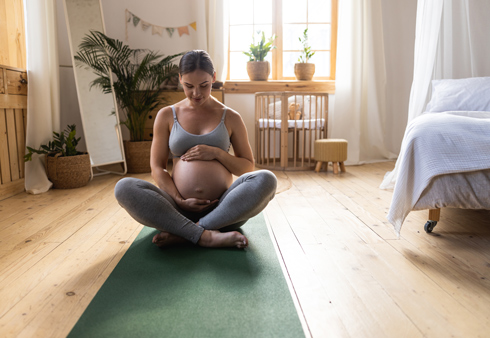 pregnant woman sitting on yoga mat, practicing mindfulness in a serene room with natural light and plants, promoting wellness during pregnancy