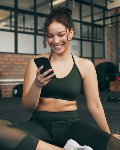 smiling woman in athletic wear sitting on the gym floor looking at her phone